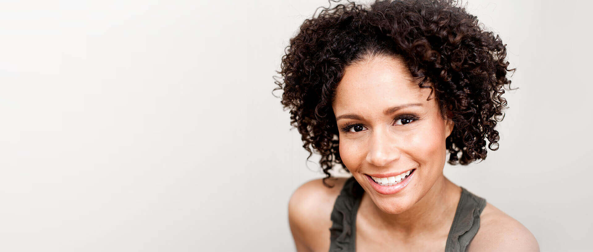 Smiling person with curly hair, wearing a sleeveless top, representing patient-centered care at The Dental Specialists.